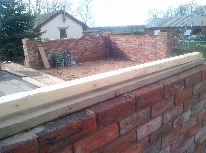 A new brick retaining wall with stone coping running across the back of a house