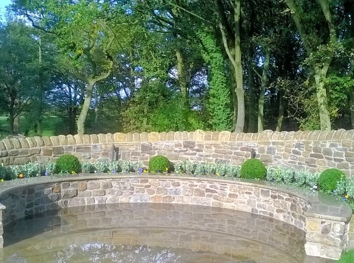 A long curved stone retaining wall with clipped box balls and planting, set in front of mature trees