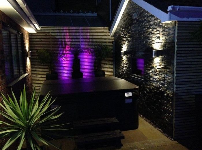 A planted garden lit at night, with uplighting through the shrubs and a seating area beyond