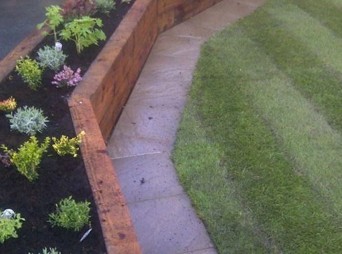 A newly planted border edged with sleepers alongside a freshly cut lawn and path