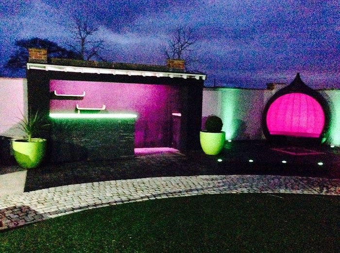 An outdoor kitchen and bar area lit at night beside a lawn and paving