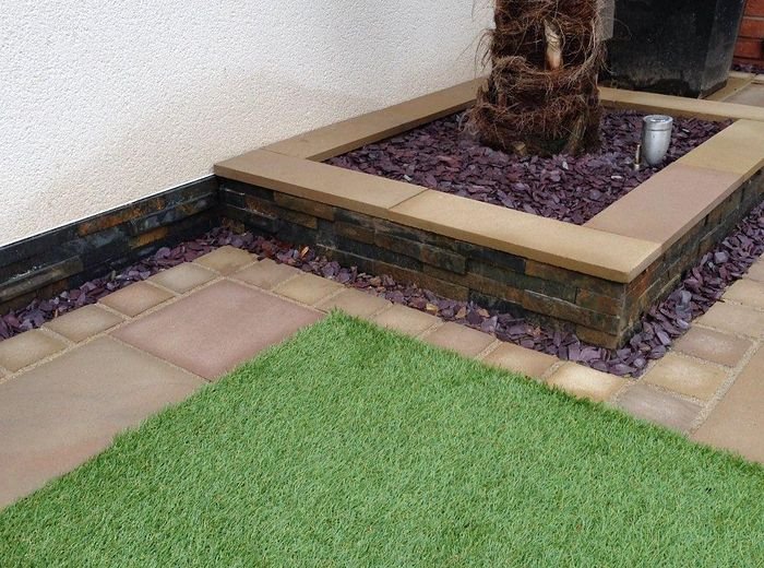 A patio corner with artificial lawn, a sleeper-edged bed and a timber feature