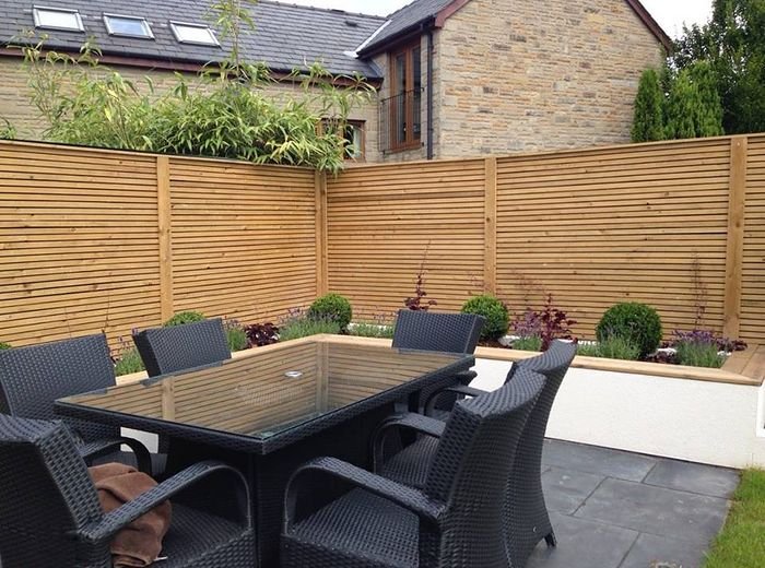 A paved seating area with a rattan dining set against new timber fencing