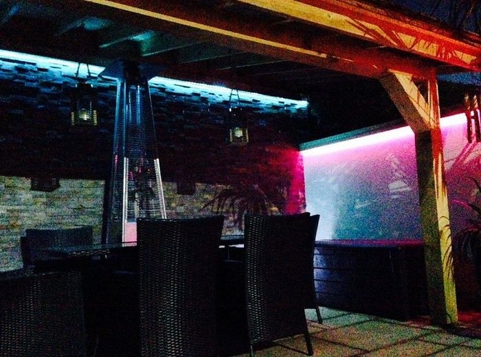 A pergola seating area lit with colour-changing lights above rattan furniture