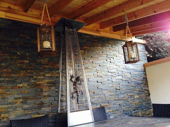 A covered pergola with a stone feature wall, lanterns and a patio heater