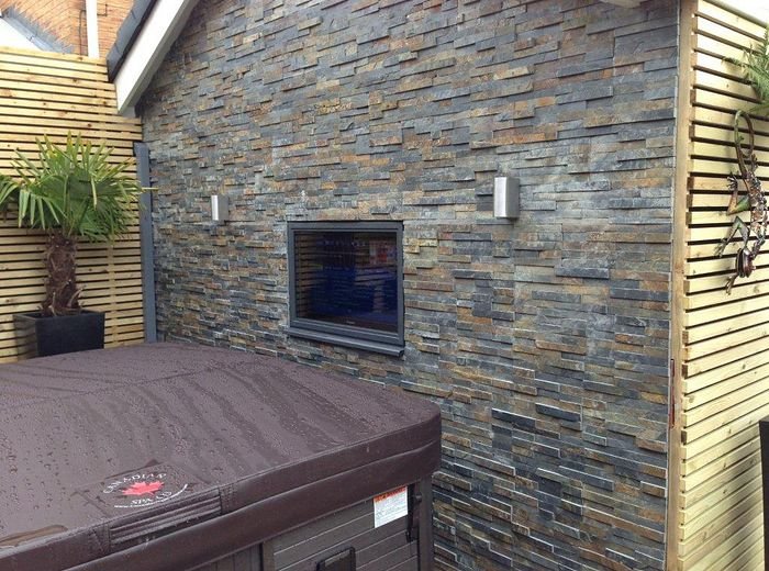 A stone wall with a built-in fire and a sunken hot tub on a lit terrace