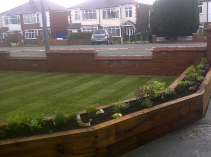 A freshly mown lawn with mower stripes and a newly built sleeper border at the front of a house