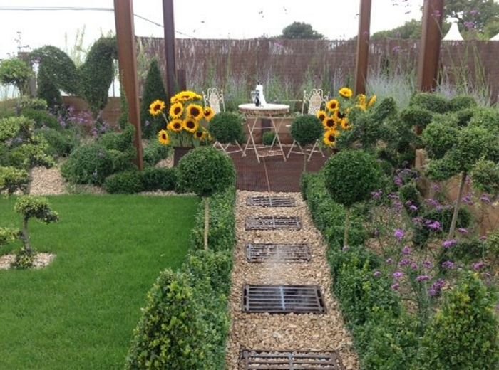 A garden path lined with topiary, sunflowers and deep planted borders
