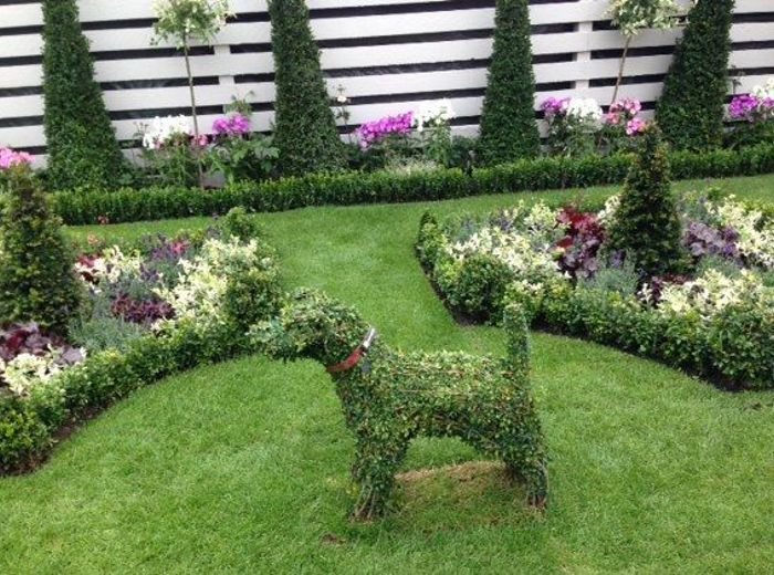 Topiary cut into animal figures on a lawn framed by clipped hedging and white slatted fencing