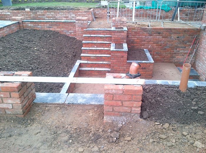Brick retaining walls and steps part-built, with the ground still to be levelled