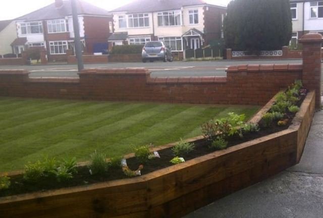 A freshly mown lawn with mower stripes, edged against a new sleeper border at the front of a house